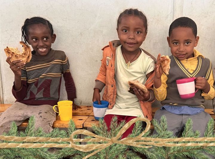 Ethiopian children sitting on benches eating Berta pancakes 